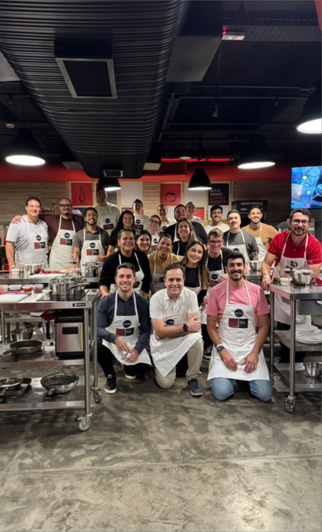 Participantes de evento corporativo posando para foto em grupo na cozinha.